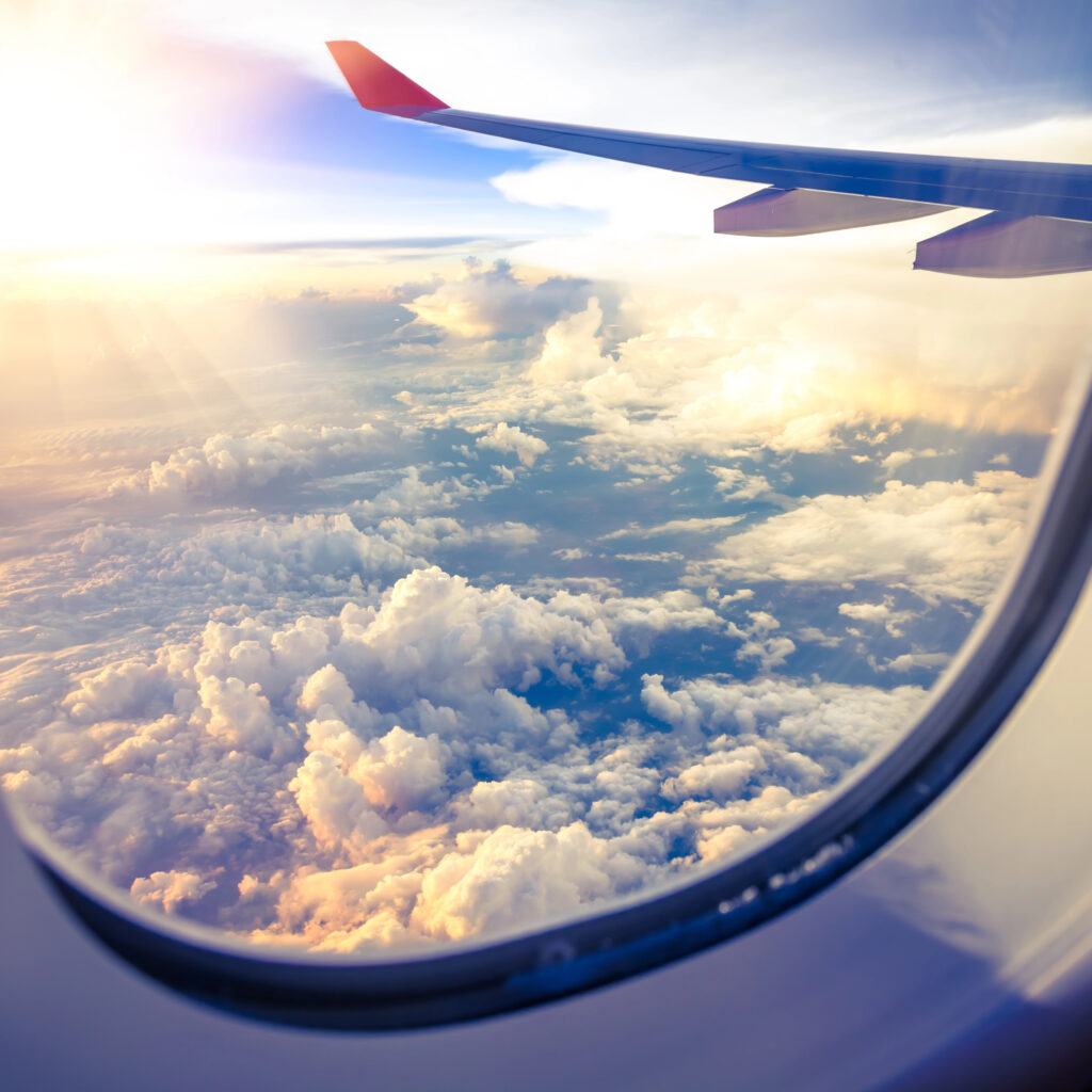 Airplane wing over clouds at sunset, ideal for exploring Hawaii and Hawaii travel on a budget.